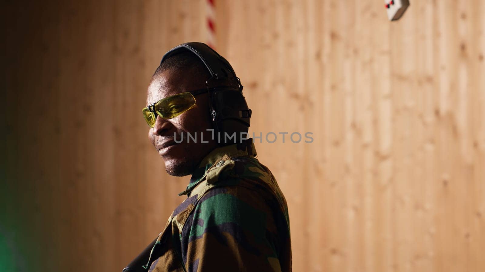 Portrait of happy military personnel using tactical operations equipment, shooting assault rifle. Smiling man in firing range preparing for mission, practicing with semiautomatic weapon, camera B