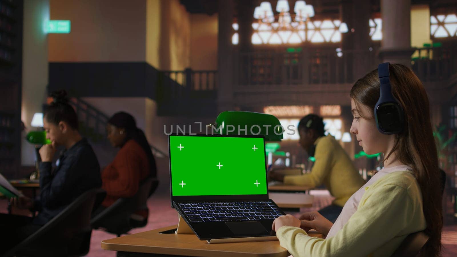 Focused schoolgirl engaged in academic tasks with green screen at a library, working on school assignments with her laptop. Solving class work tasks, searches information on internet. Camera A.