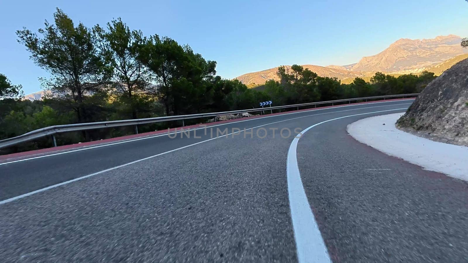 A winding road winds through majestic mountains, lush greenery, and clear blue skies, ideal for adventurers