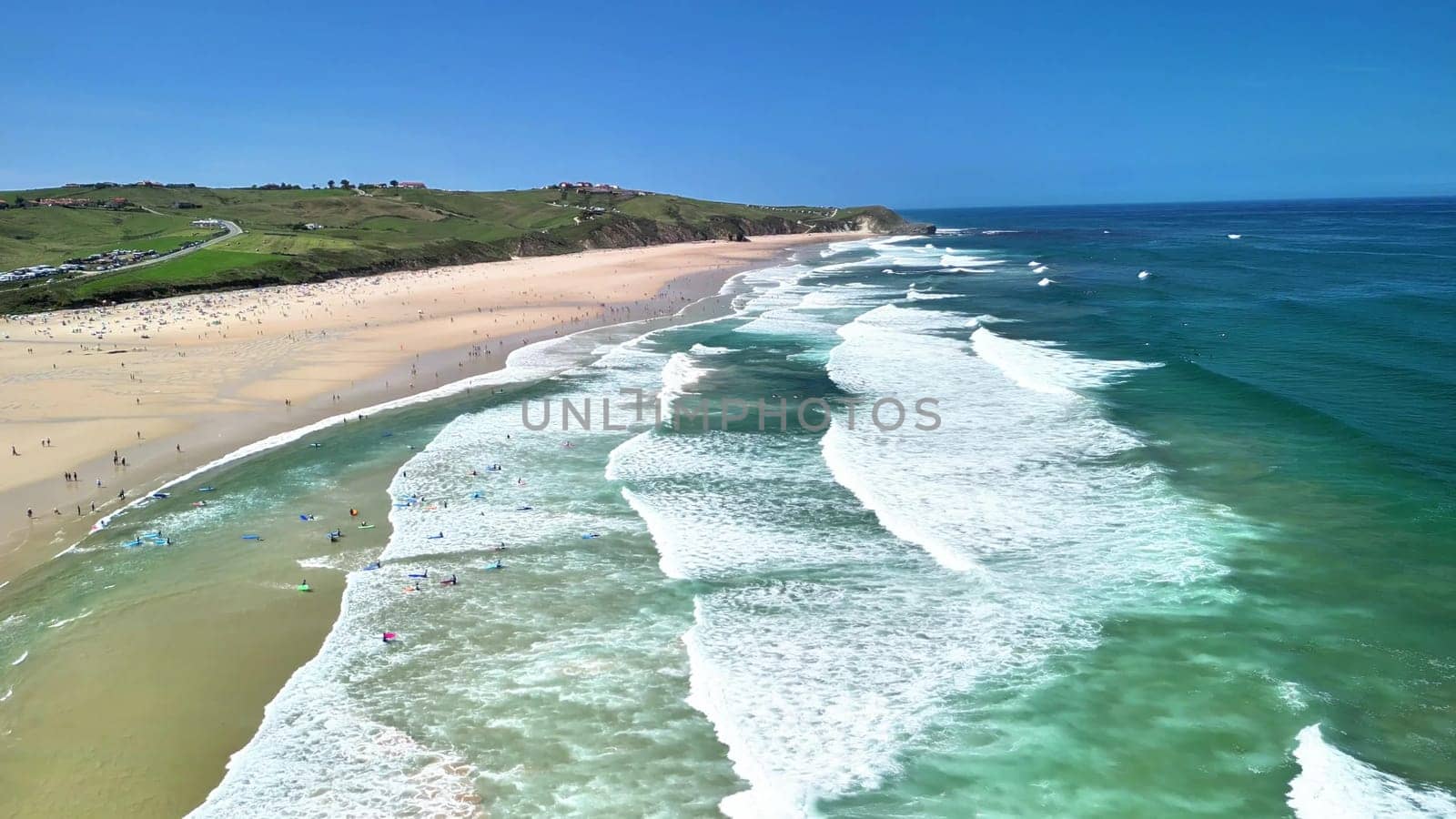 Breathtaking aerial shot showcasing a beautiful beach, gentle waves, and surfers enjoying the water.