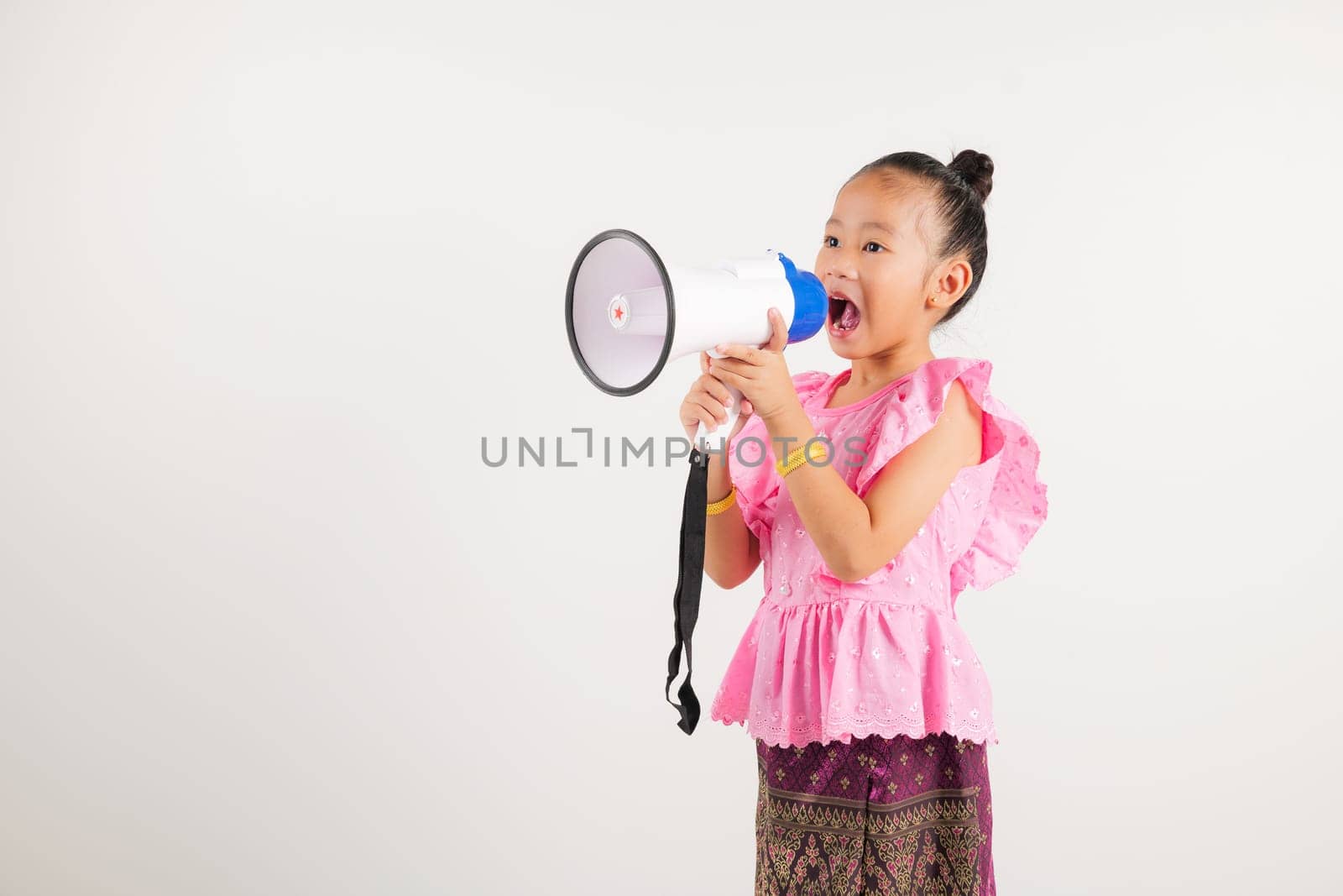 Portrait Thailand kid girl smiling traditional Thai dress costume shouting by megaphone, studio shot isolated white background, kindergarten screeching through in megaphone announces discounts
