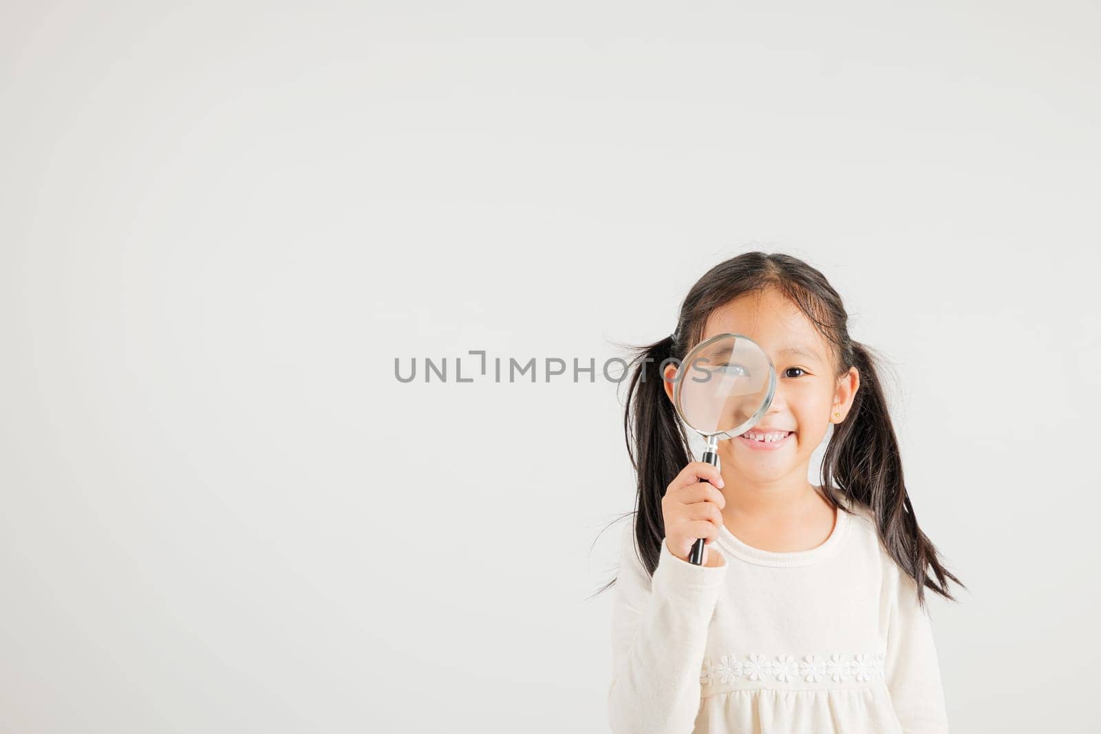 Asian little kid girl funny looking through magnifying glass at studio shot isolated on white background, Happy kindergarten child lifestyle smiling exploring holding magnifier searching, Education