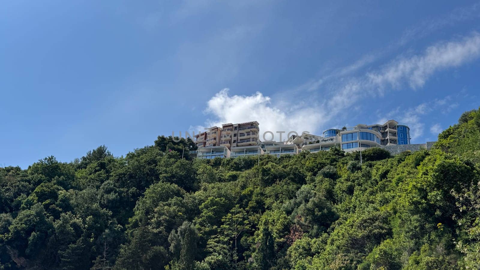 Budva, Montenegro - May 18, 2025: Luxury apartments perched on hillside amidst vibrant green trees and clear blue sky