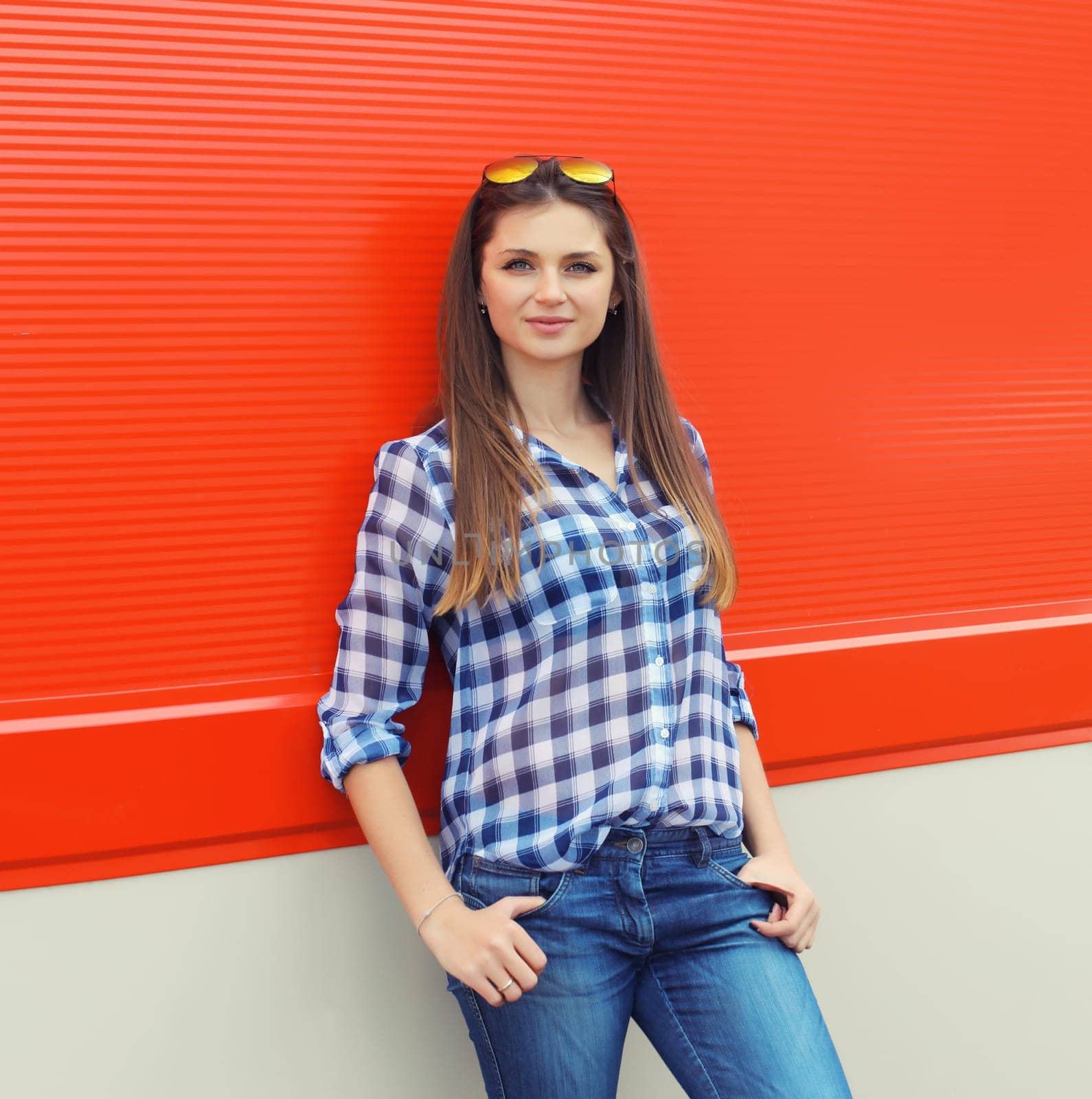 Portrait of beautiful smiling brunette young woman with glasses in casual clothing posing on colorful red wall background