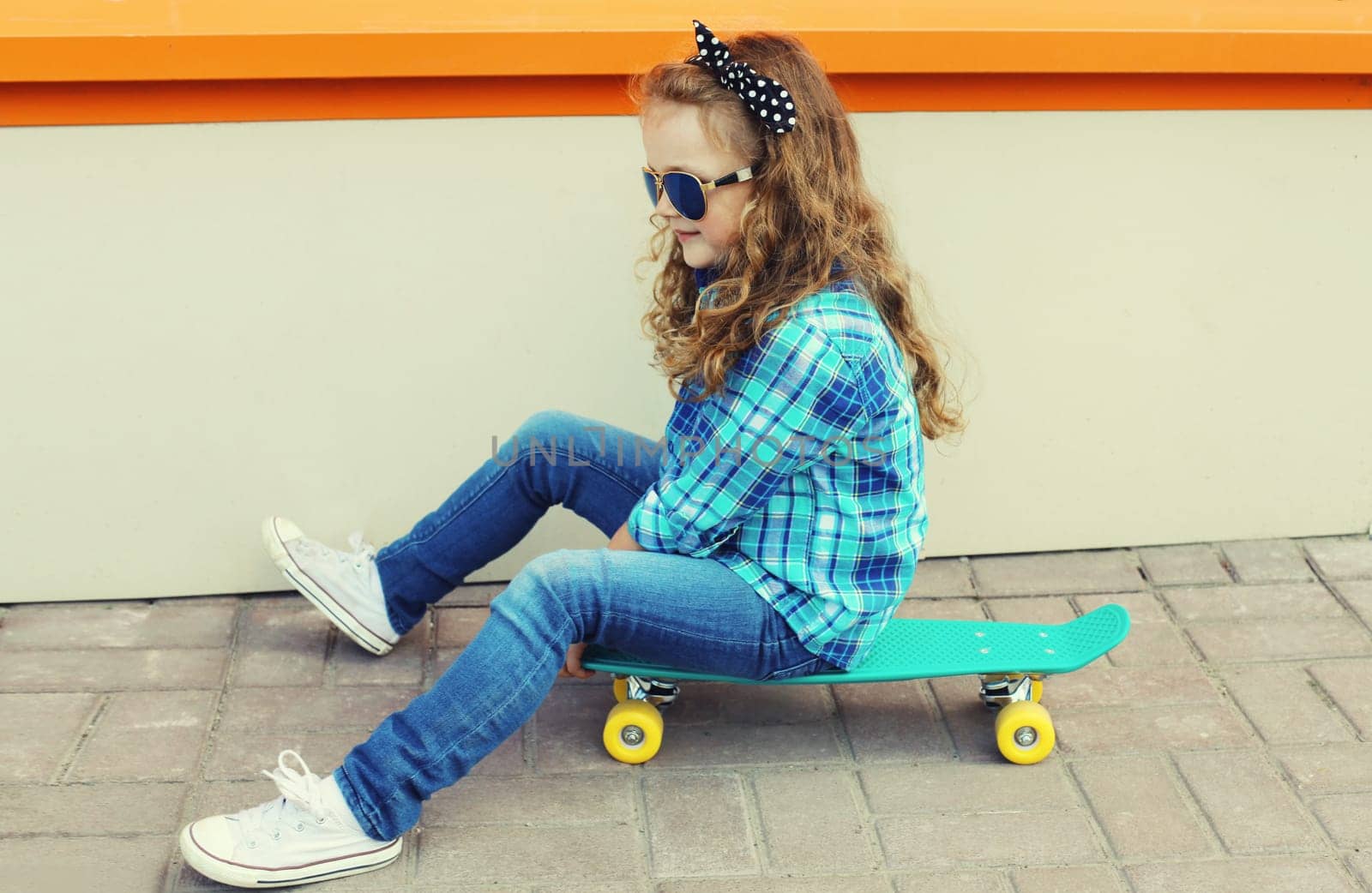 Portrait of stylish little girl child posing with skateboard on city street