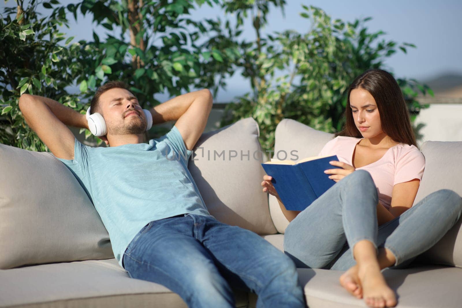 Couple relaxing spending time in different ways reading book and listening music in a terrace
