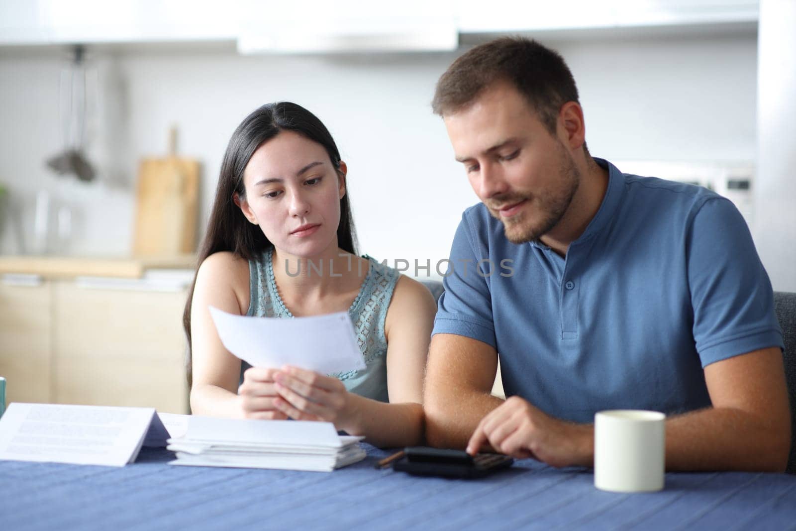 Interracial couple calculating expenses reading bill in the kitchen at home