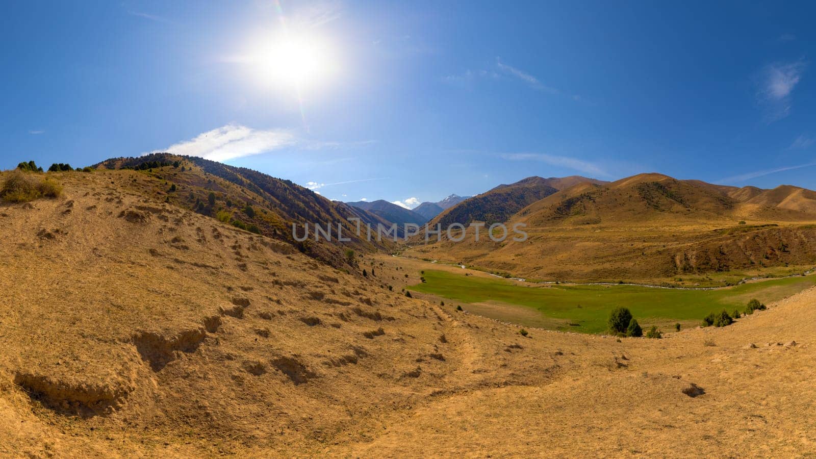 dry dust covered hill in mountains with blue sky and sun above at autumn day in Kyrgyzstan
