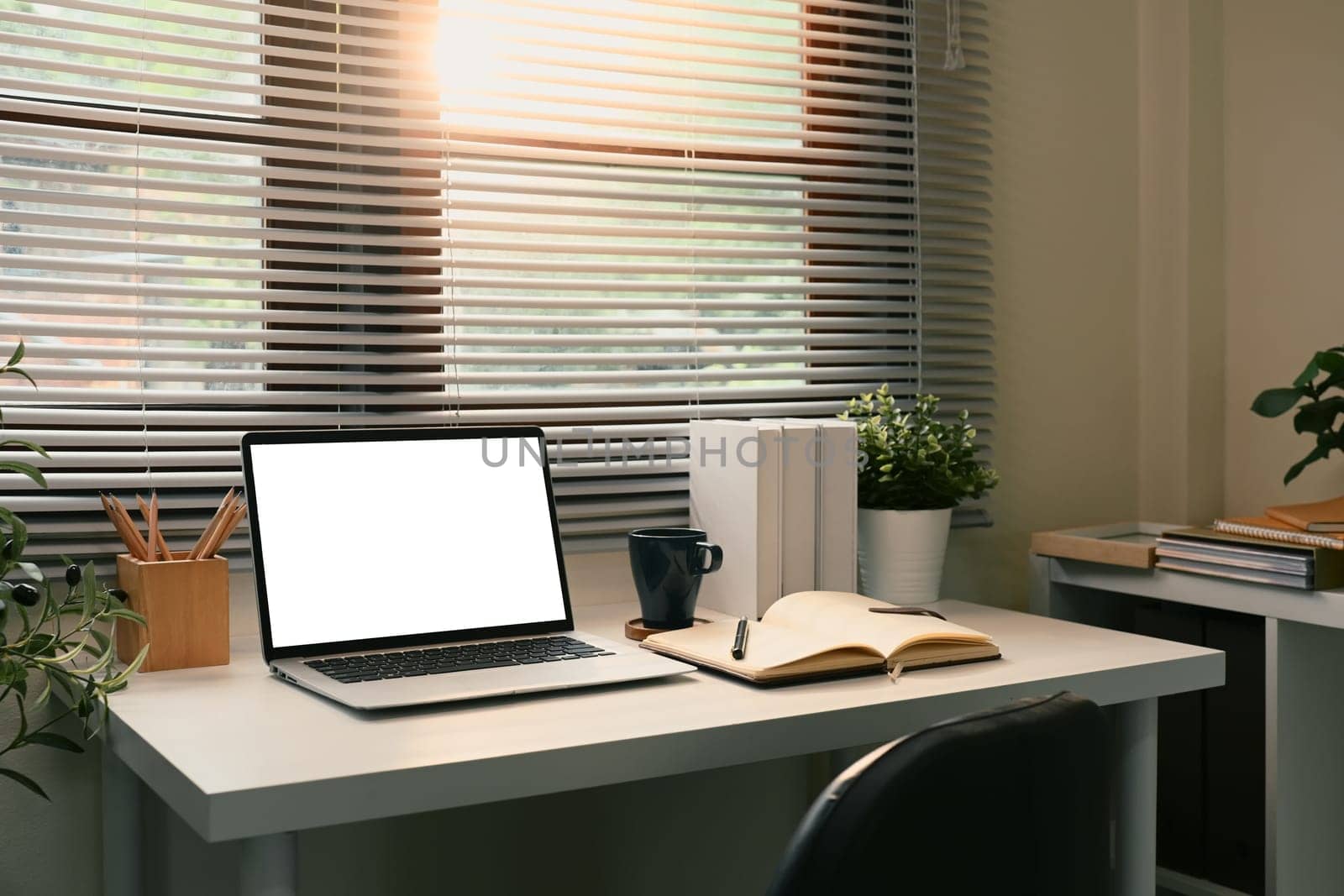 Laptop with blank screen by the window with soft sunlight streaming through blinds.