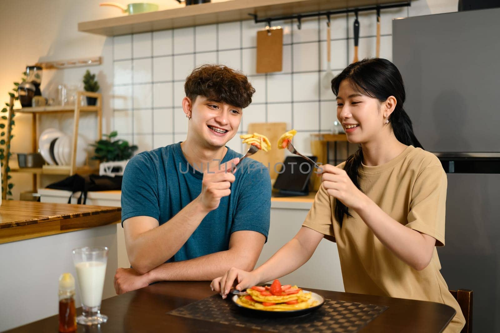 Romantic couple enjoying pancake breakfast together in a cozy kitchen.