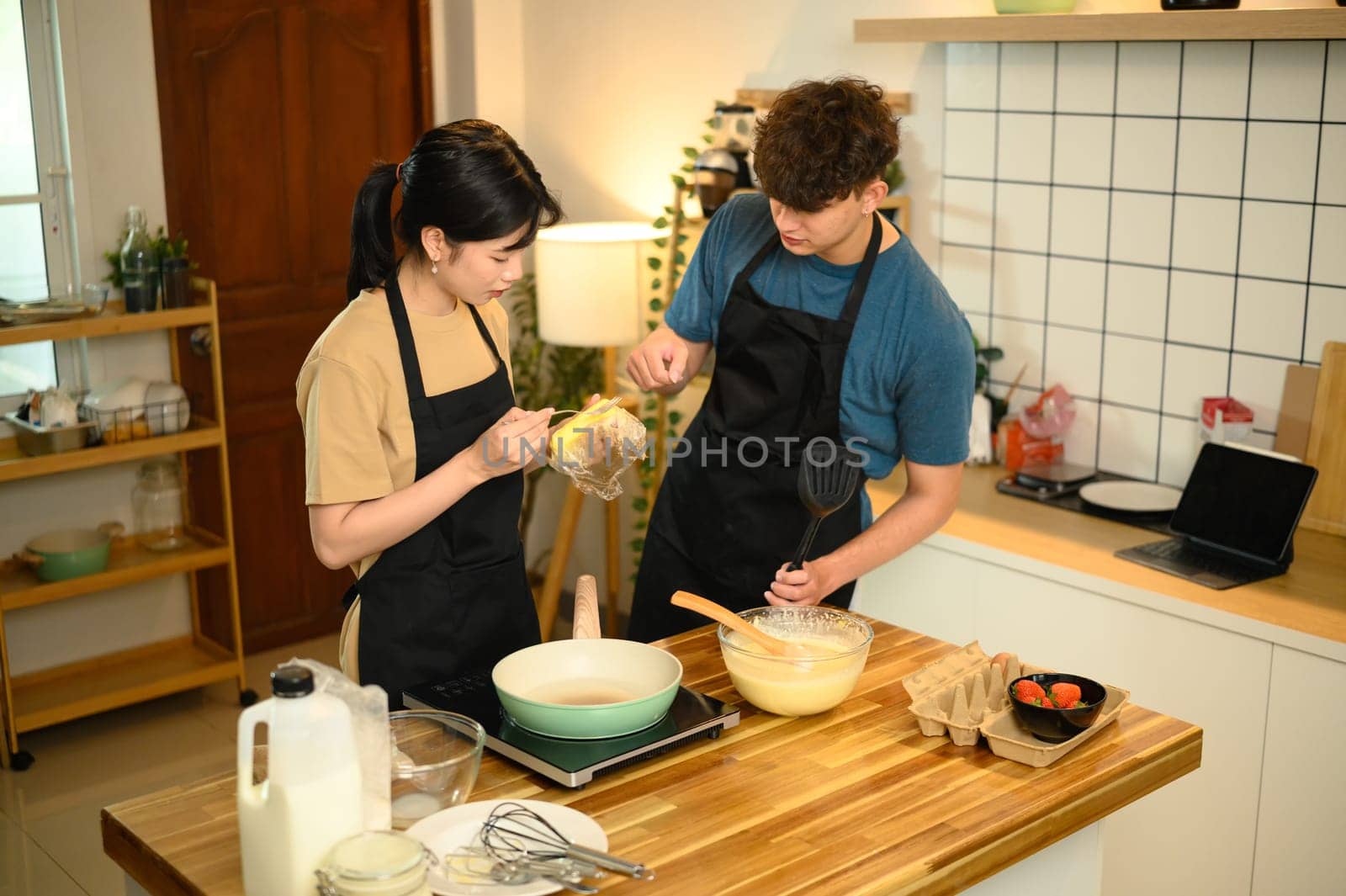Happy couple preparing homemade pancakes in a warm kitchen.