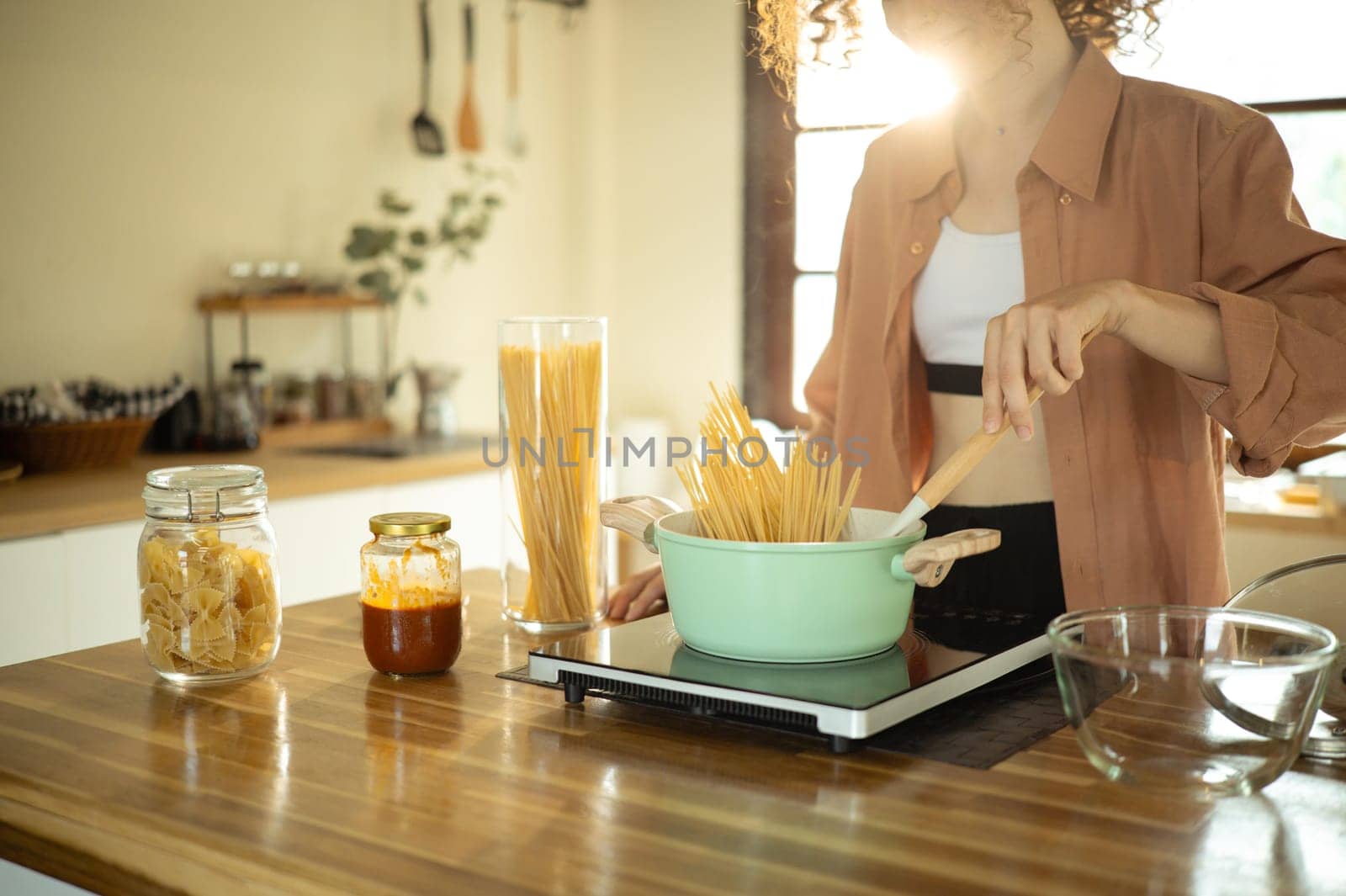 Young woman with curly hair prepares spaghetti in modern home kitchen.