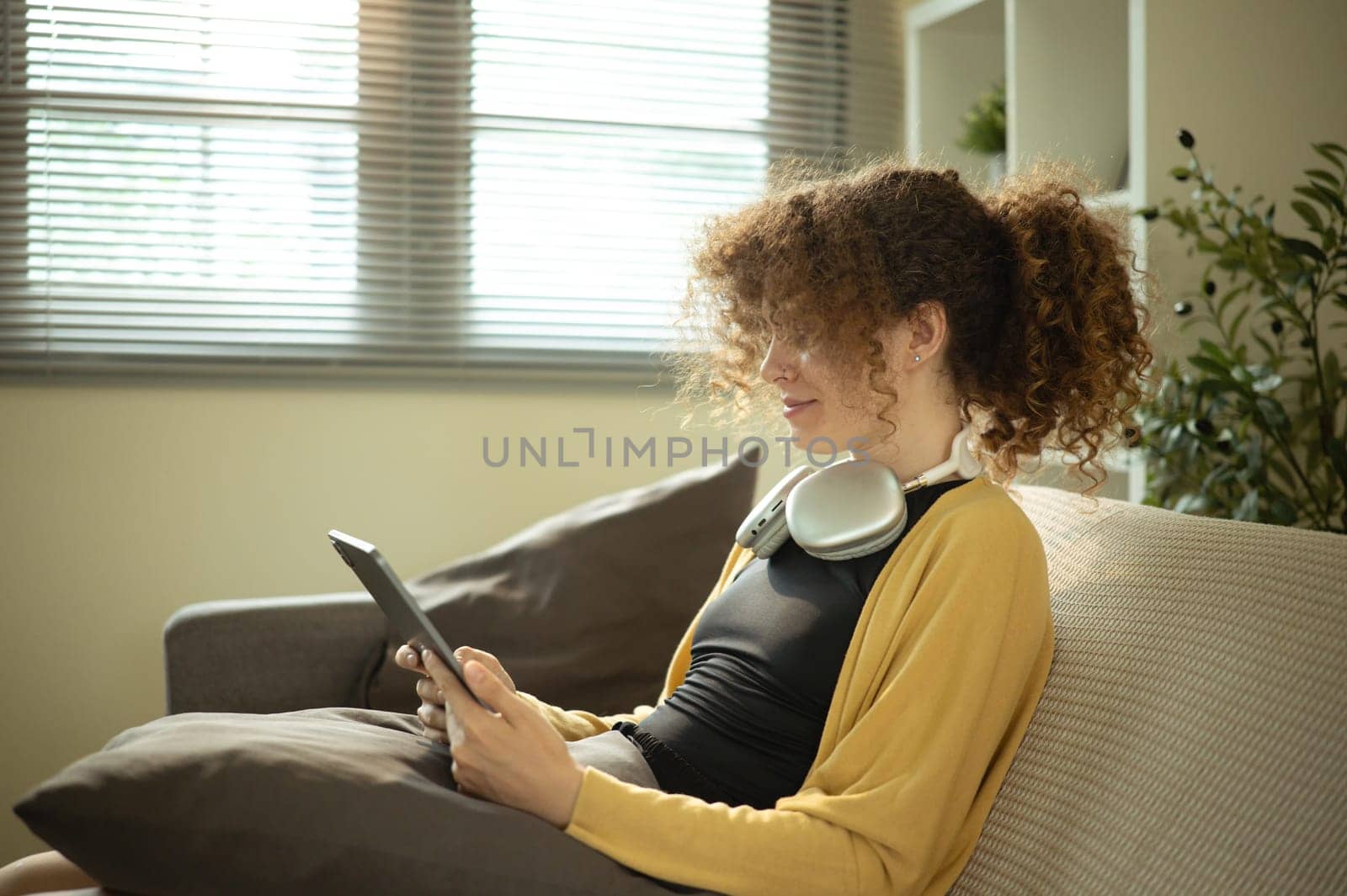 Relaxed woman in casual clothes using digital tablet while lounging at home.