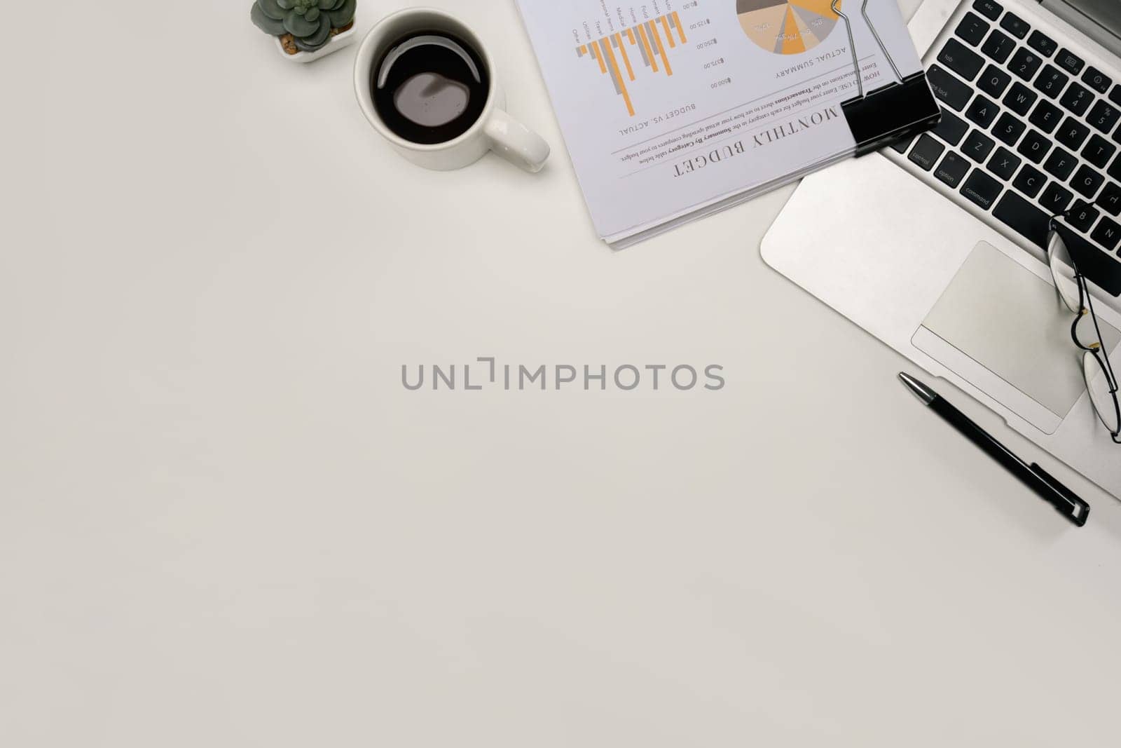 Top view of modern office desk with financial report, laptop, coffee cup, and glasses.