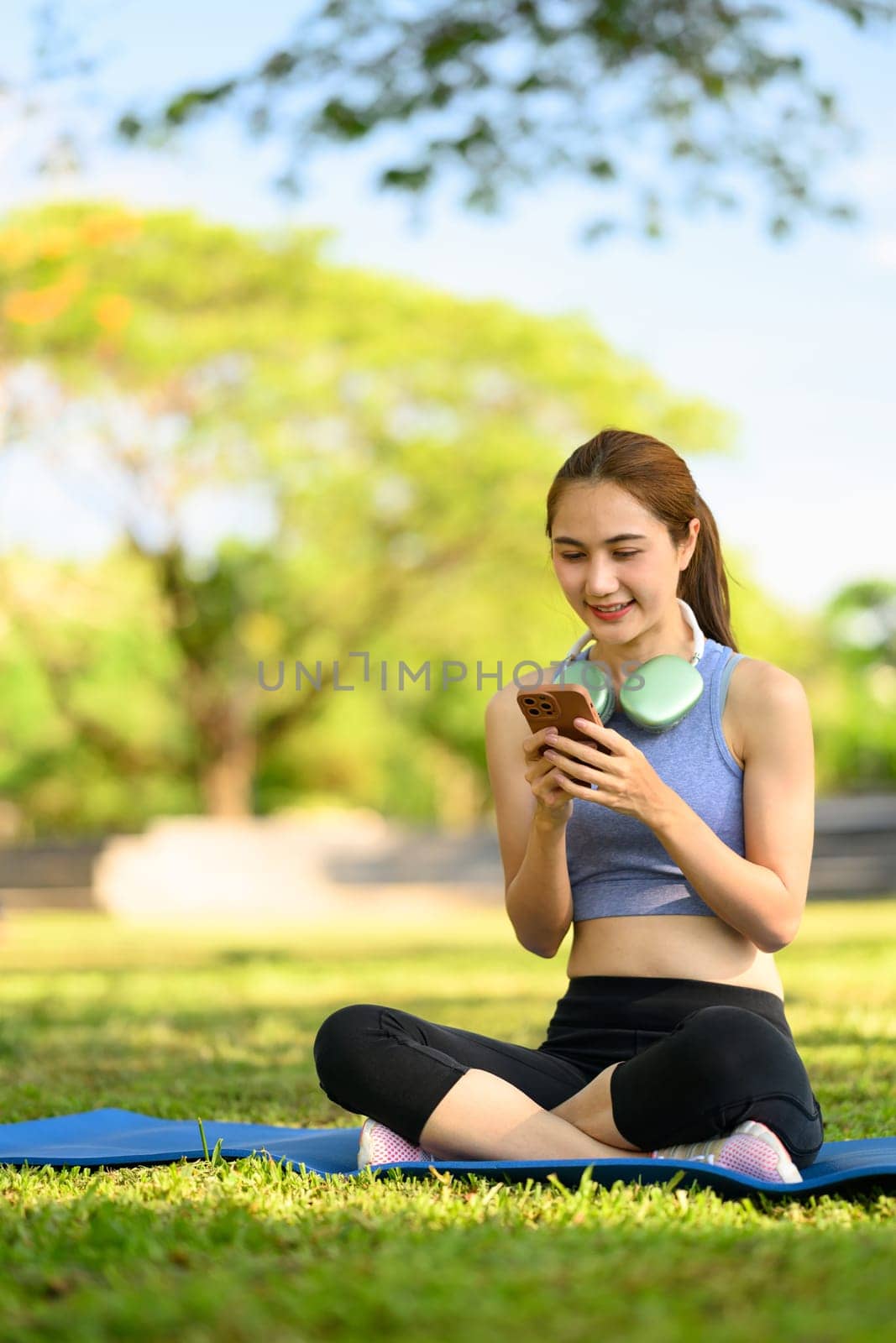 Sporty young woman uses her phone during a break in the park.