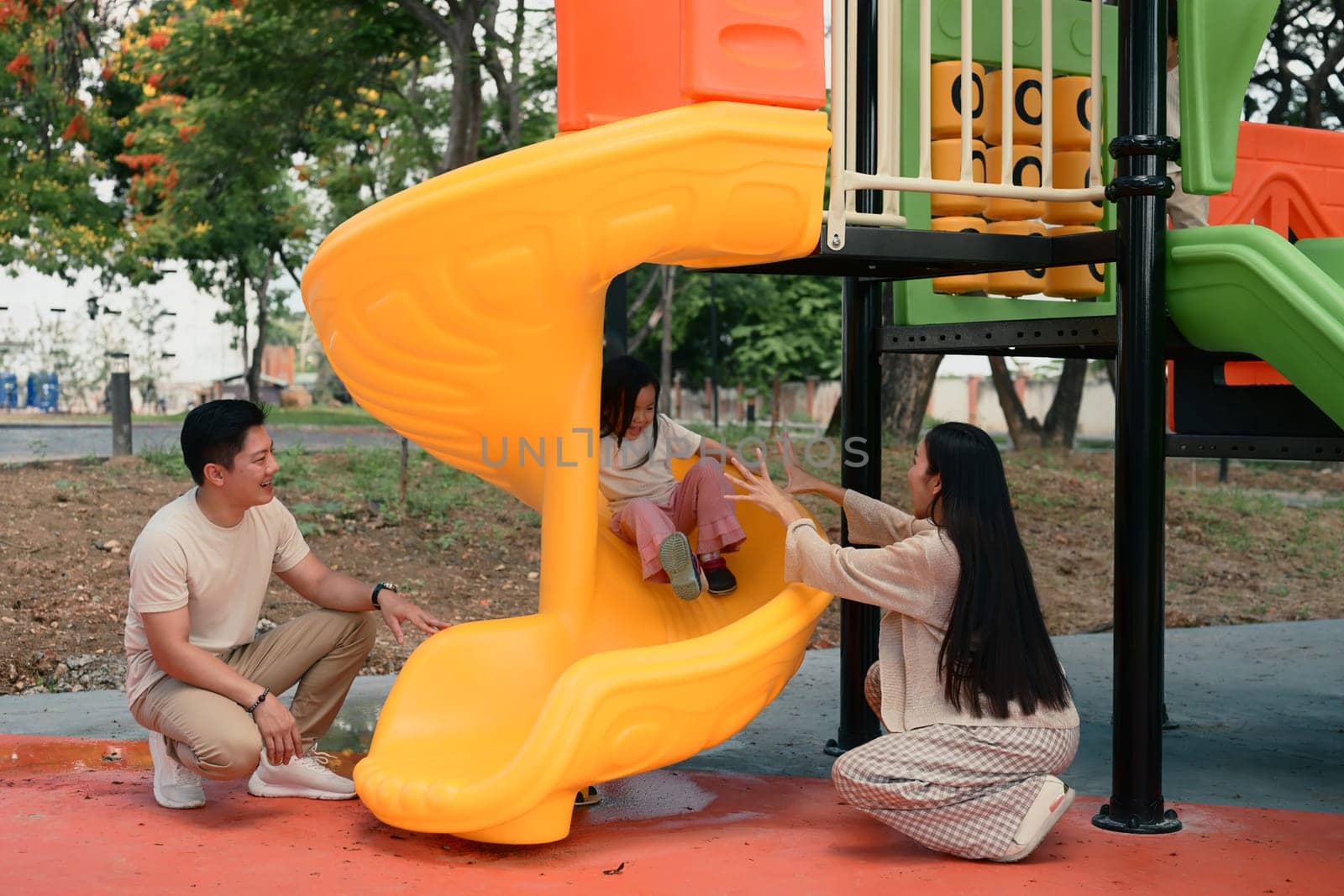 Joyful little girl enjoys sliding with support from her loving parents on both sides.