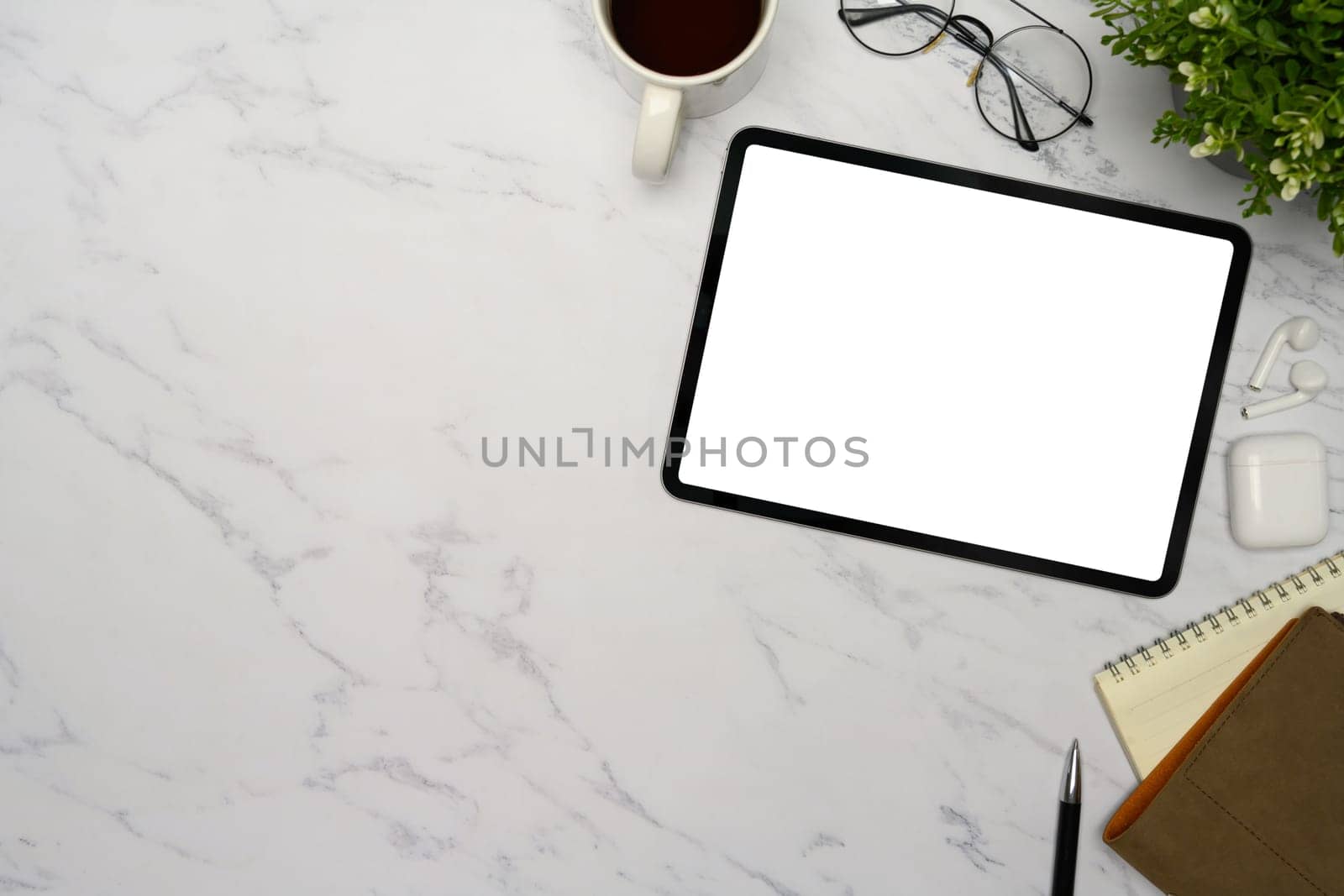 Flat lay of digital tablet with blank screen, coffee mug, notebook, and glasses on marble desk.