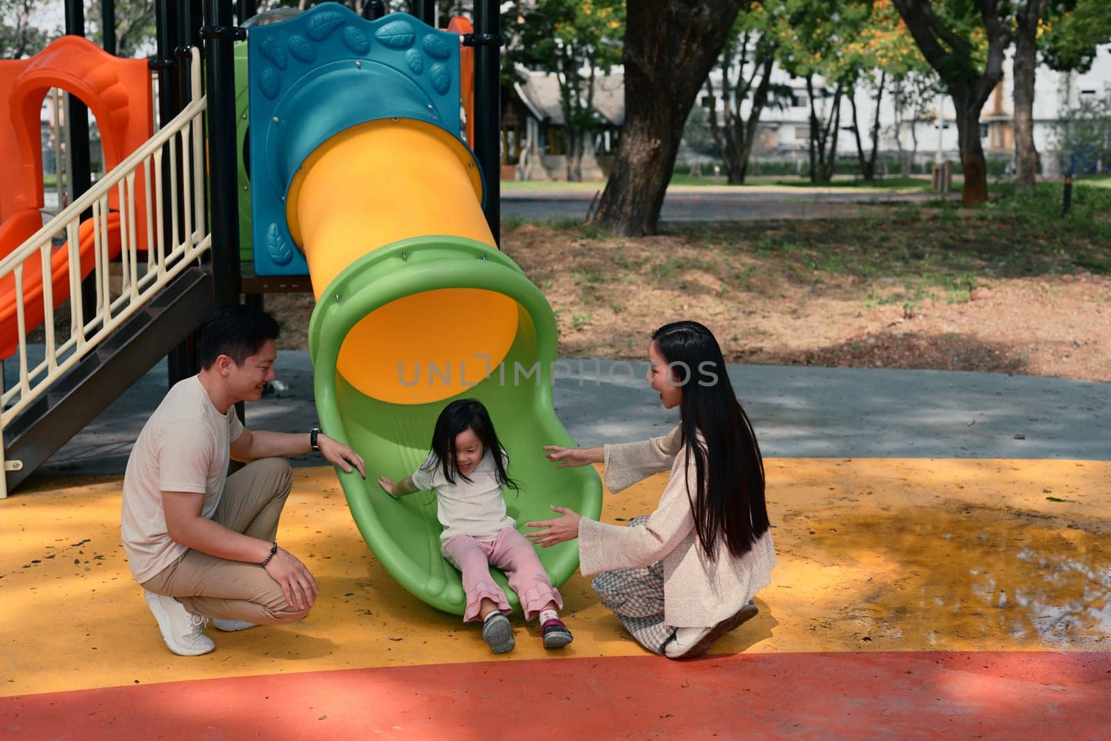 Joyful little girl enjoys sliding with support from her loving parents on both sides.