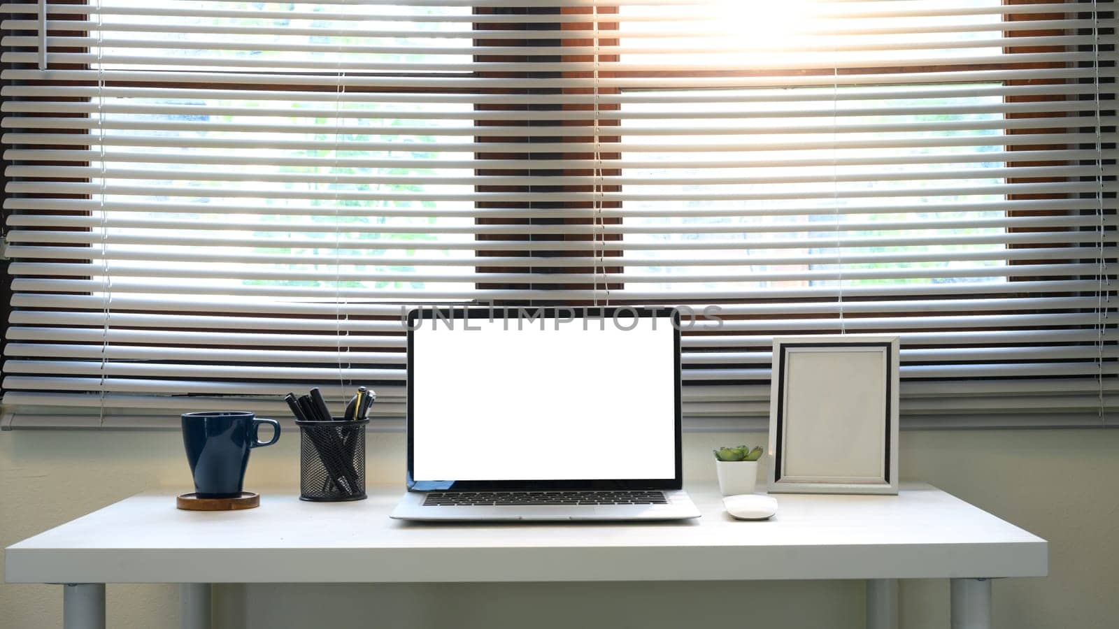 Contemporary home office desk with blank laptop screen in front of large window blinds.