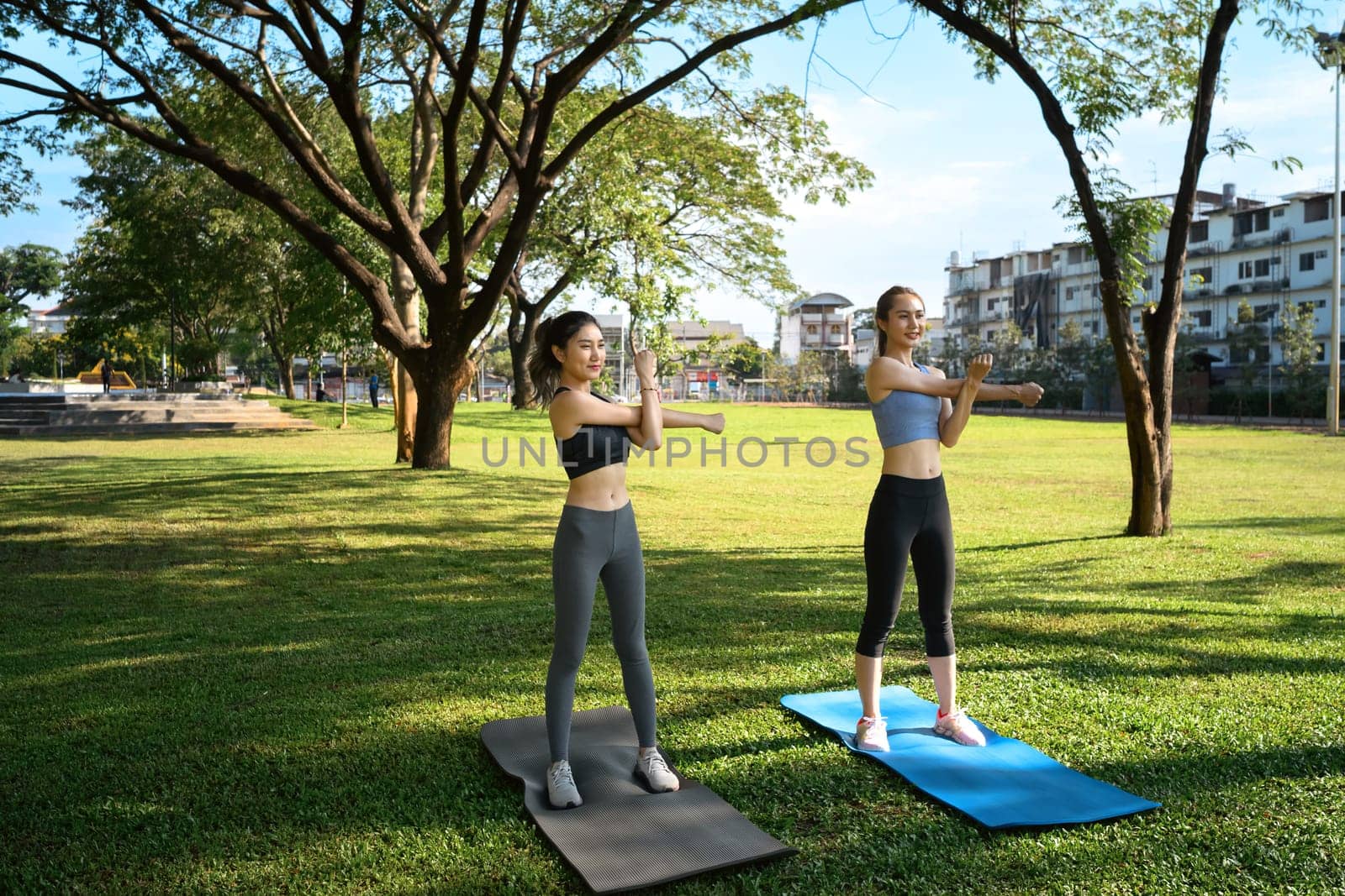 Two young women stretching outdoors on yoga mats in a city park.