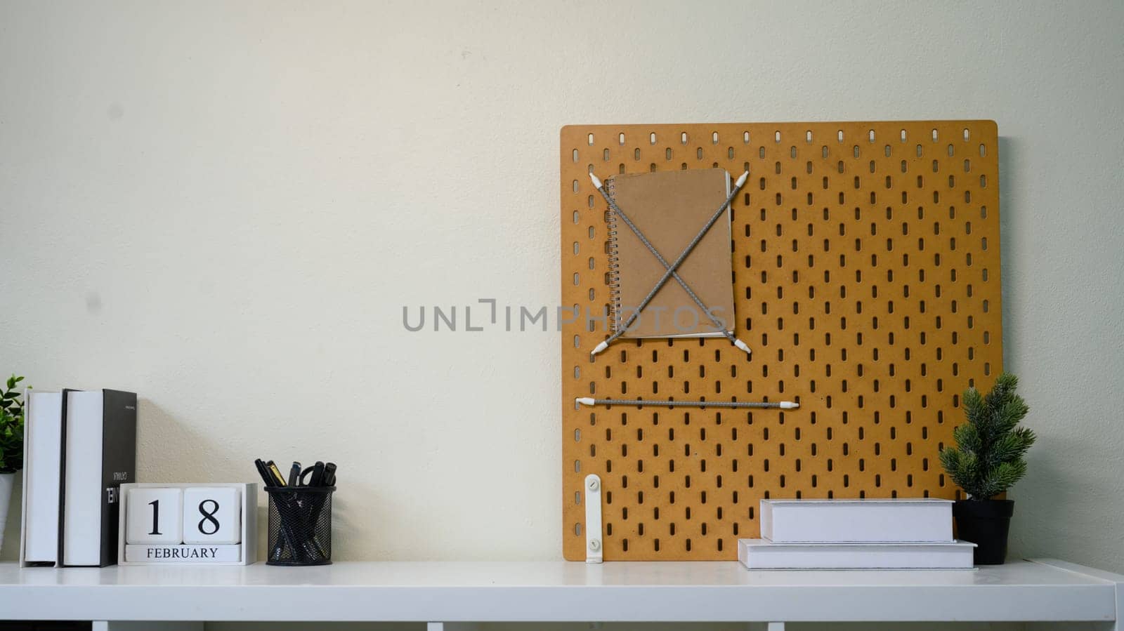 Minimalist home office shelf with pegboard, books, stationery, and indoor plants.