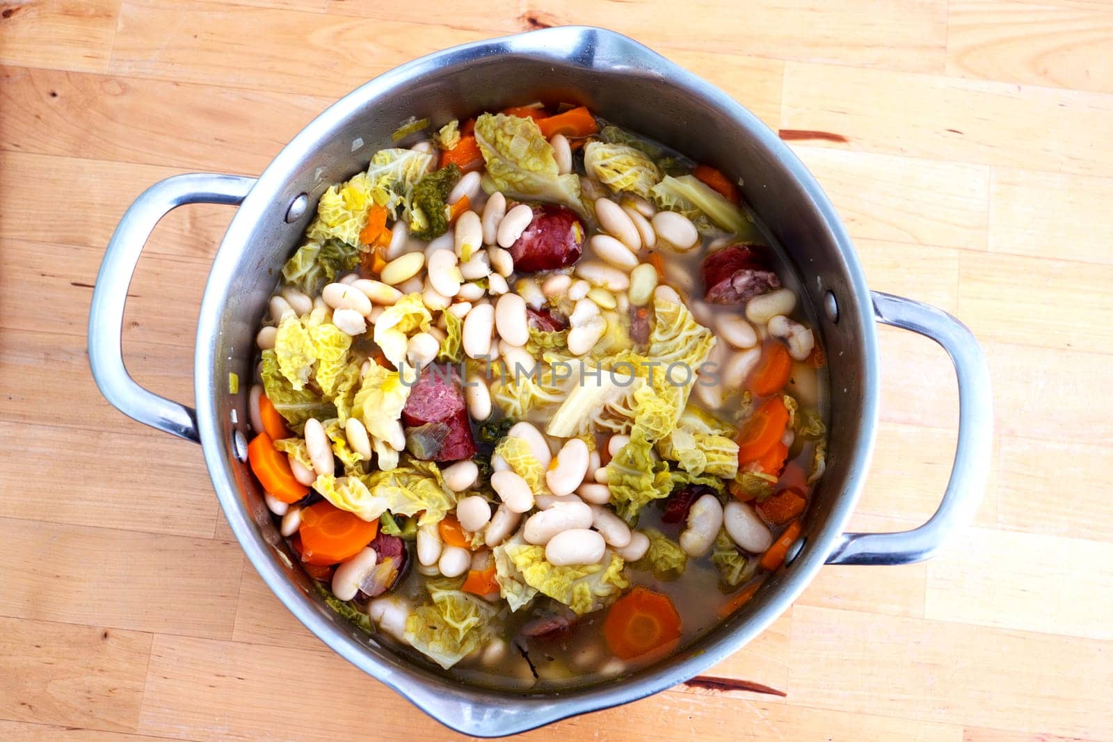 A large pot of soup with beans, carrots, and cabbage. The soup is full and has a lot of ingredients