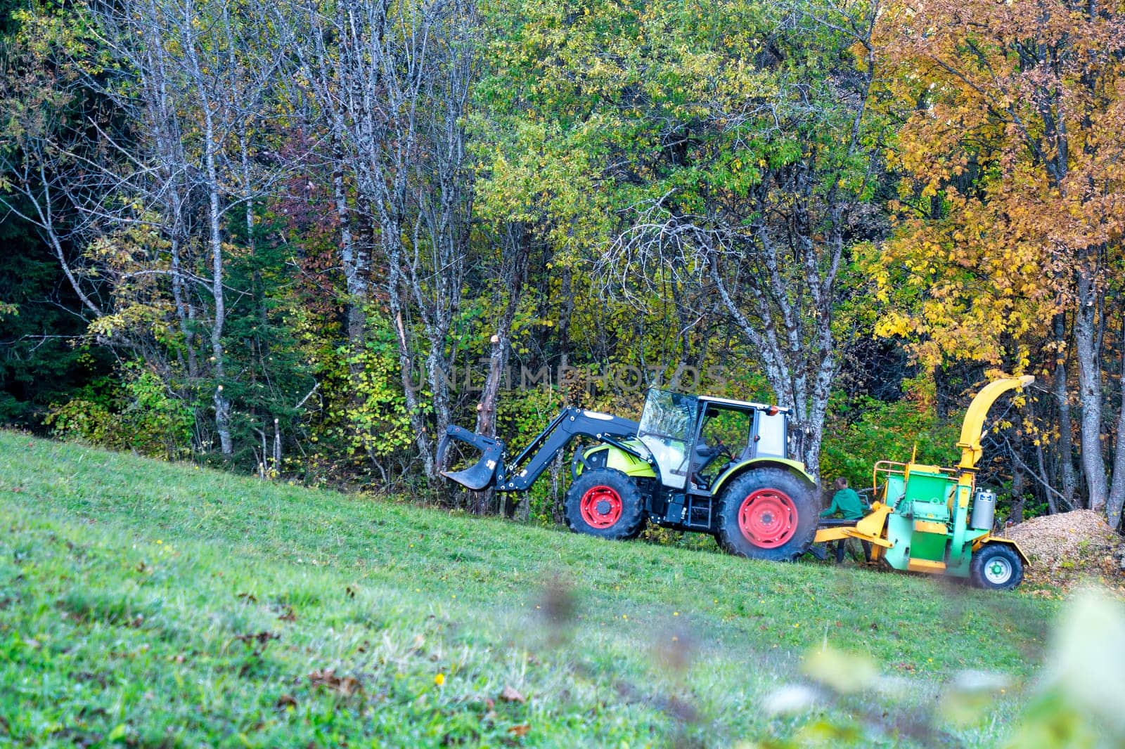 A tractor is pulling a wood chipper. The tractor is green and white