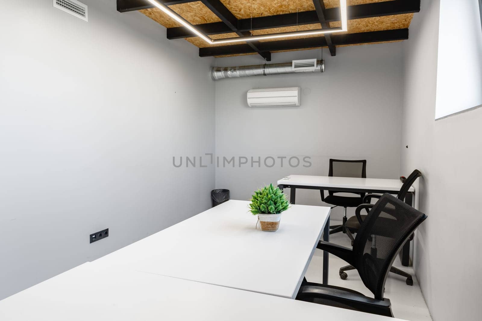 Bright and inviting workspace with sleek white desks and ergonomic chairs, perfect for productivity. Green plant adds a touch of nature to the minimalist decor.