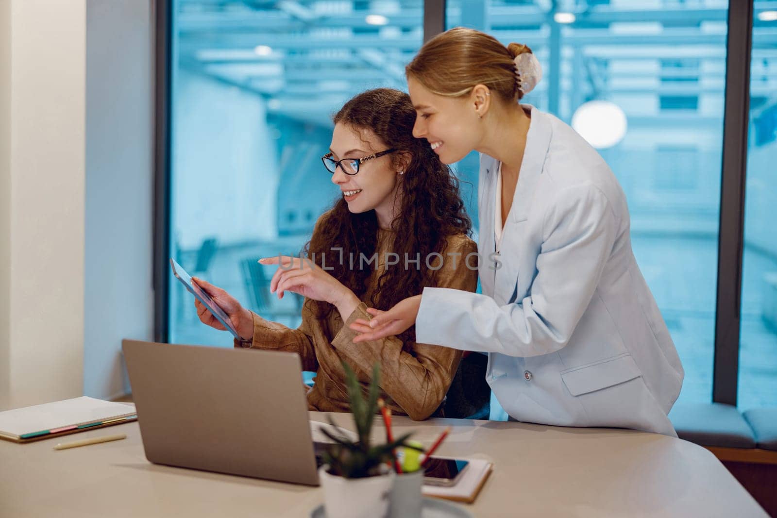 Two businesswomen are collaborating over a laptop in a modern office, showcasing the dynamics of todays workplace