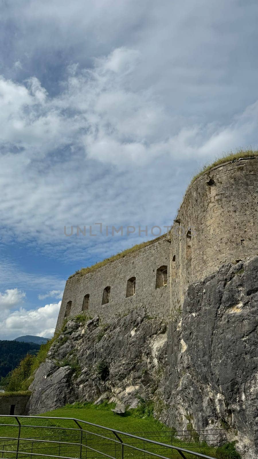 05.08.2024 Austria, Tyrol: Dramatic view of historic Kufstein Fortress wall, seamlessly built into rocky cliff. The thick stone structure with small windows blends naturally into the rugged terrain. Shot on a cloudy day, the image highlights the medieval architecture, natural textures of the rock, and the lush green grass below. Perfect for concepts of history, heritage, strength, and timeless architecture.