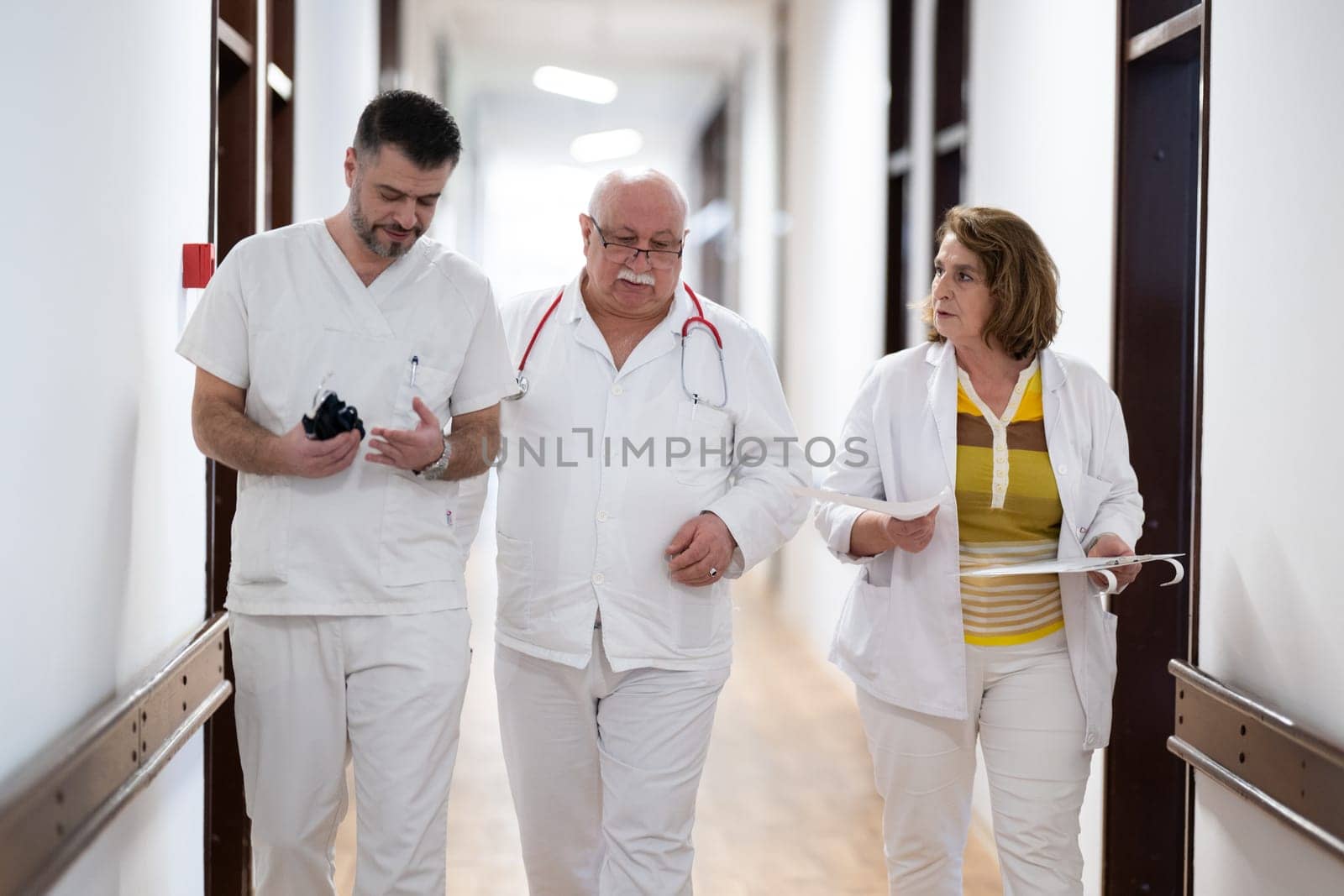 A group of healthcare professionals in white uniforms walking through a hospital hallway while reviewing patient documents and discussing treatment plans
