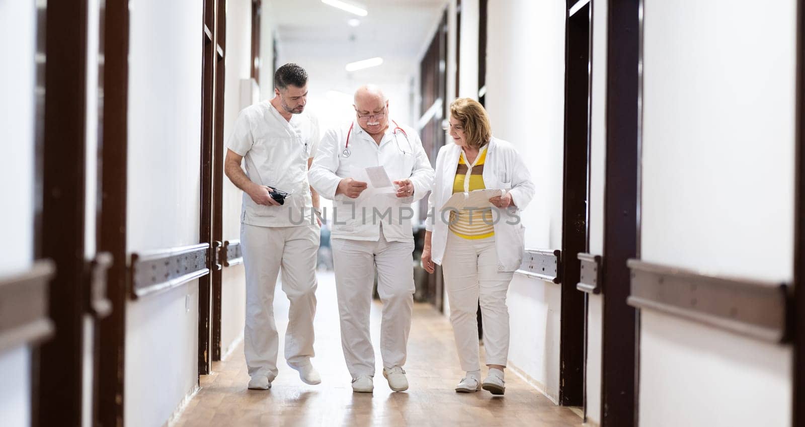 A group of healthcare professionals in white uniforms walking through a hospital hallway while reviewing patient documents and discussing treatment plans