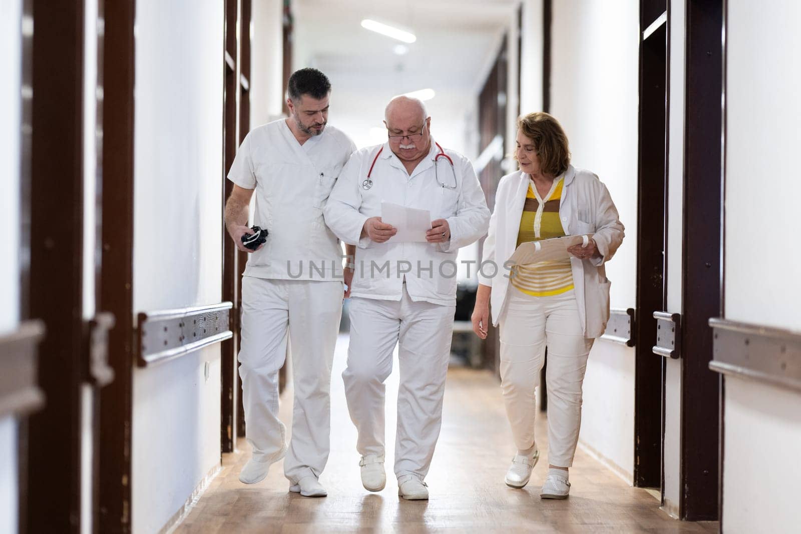A group of healthcare professionals in white uniforms walking through a hospital hallway while reviewing patient documents and discussing treatment plans