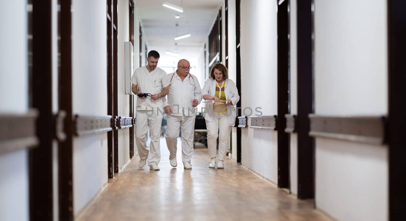 A group of healthcare professionals in white uniforms walking through a hospital hallway while reviewing patient documents and discussing treatment plans