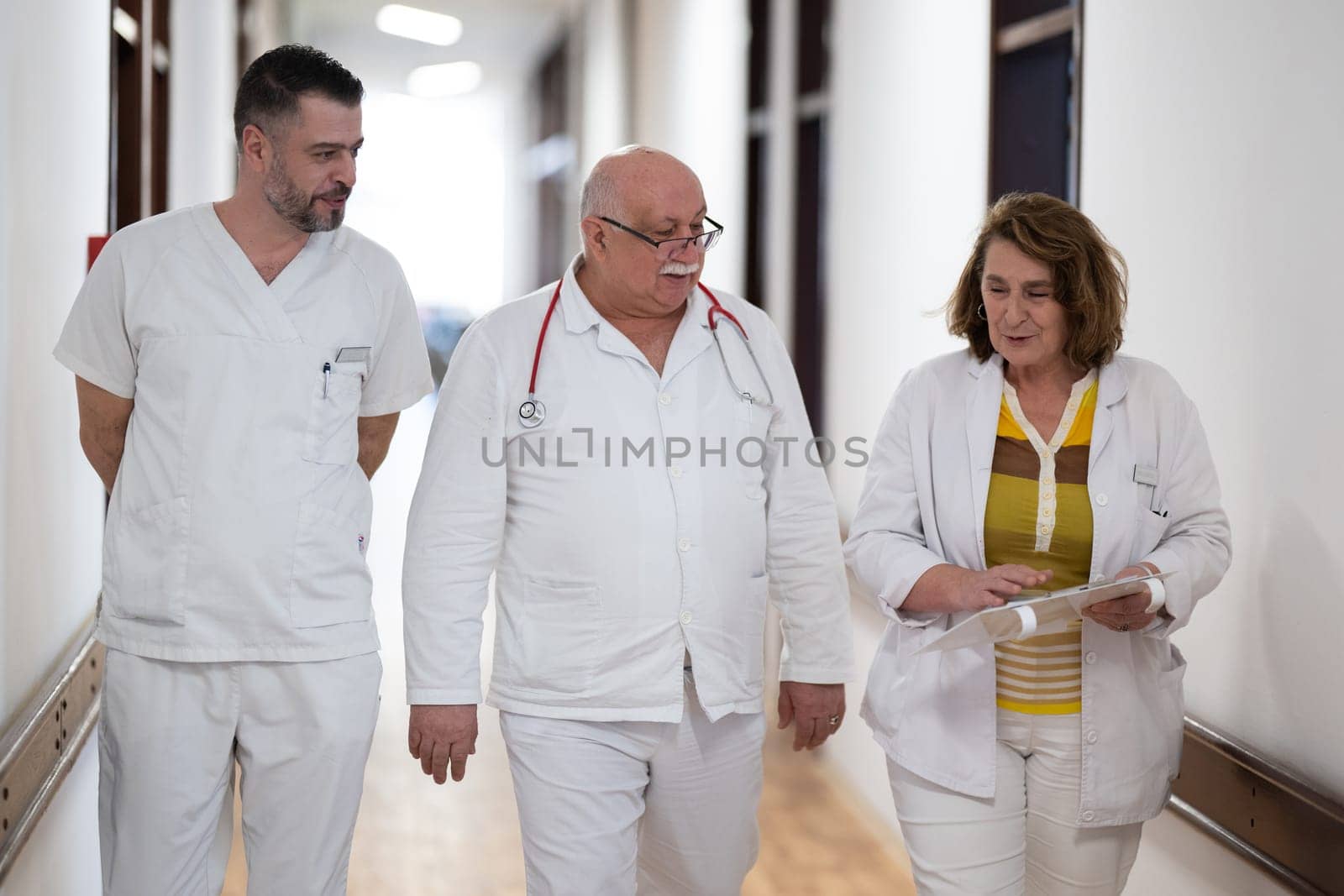 A group of healthcare professionals in white uniforms walking through a hospital hallway while reviewing patient documents and discussing treatment plans
