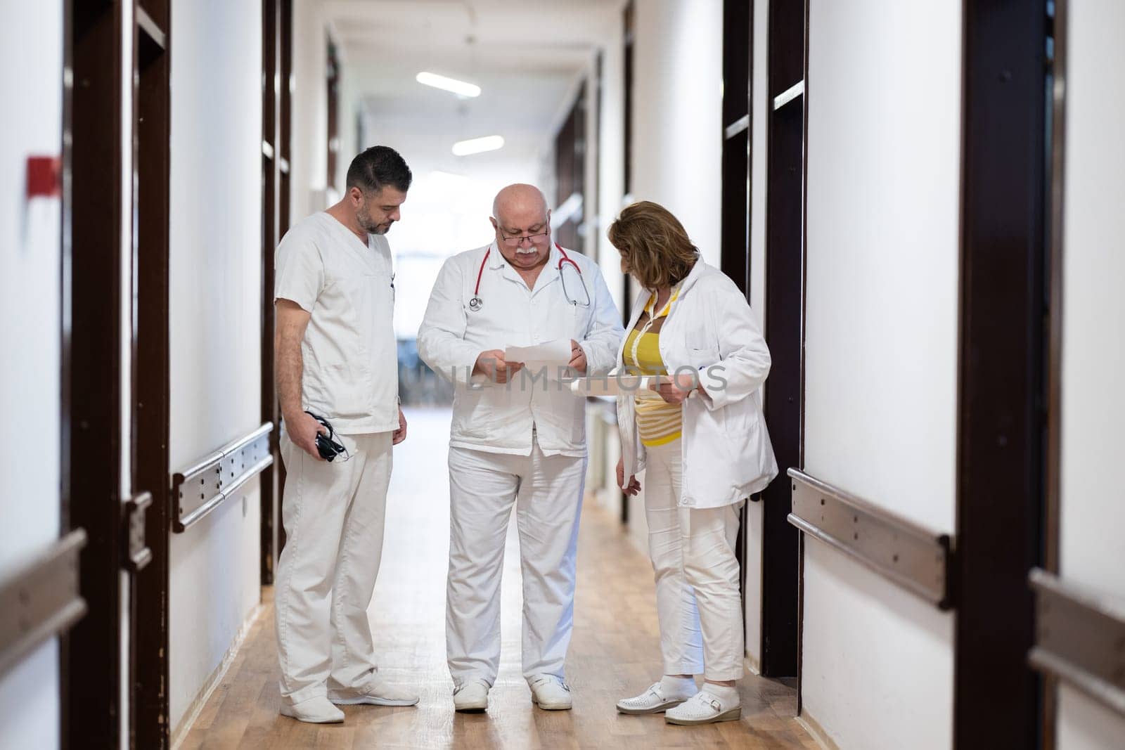 A group of healthcare professionals in white uniforms walking through a hospital hallway while reviewing patient documents and discussing treatment plans