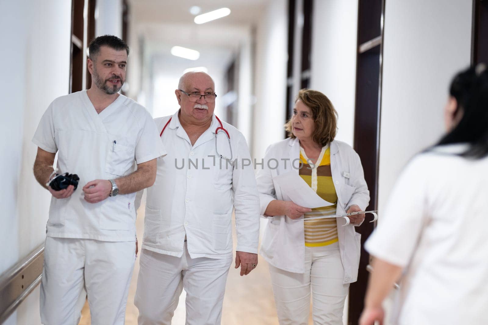 A group of healthcare professionals in white uniforms walking through a hospital hallway while reviewing patient documents and discussing treatment plans