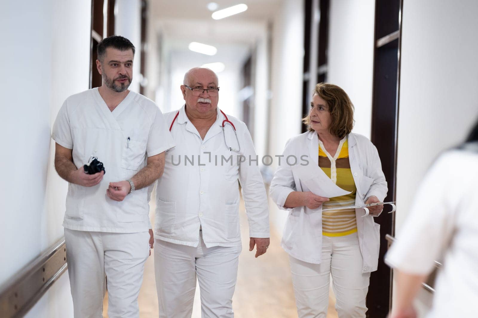 A group of healthcare professionals in white uniforms walking through a hospital hallway while reviewing patient documents and discussing treatment plans
