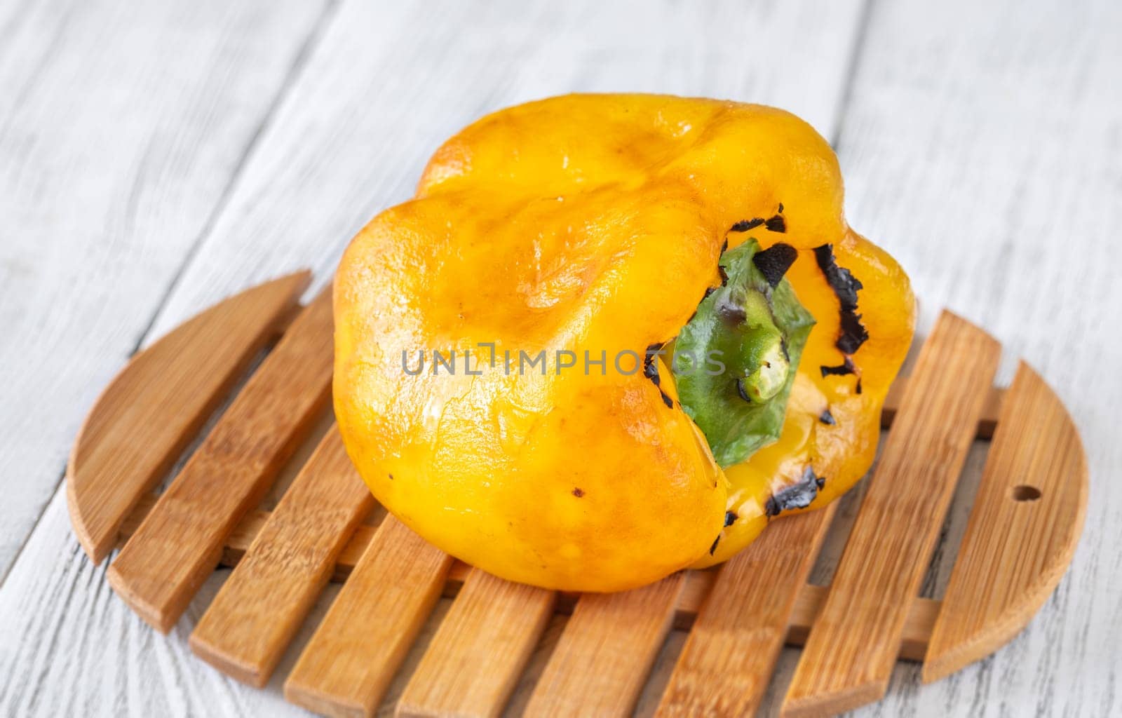 Charred yellow pepper glistens with grill marks, resting simply on aged wood