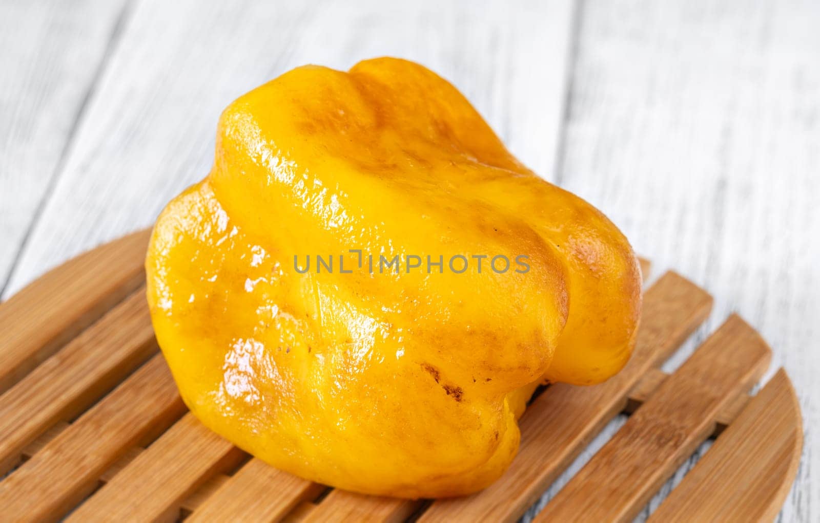 Charred yellow pepper glistens with grill marks, resting simply on aged wood