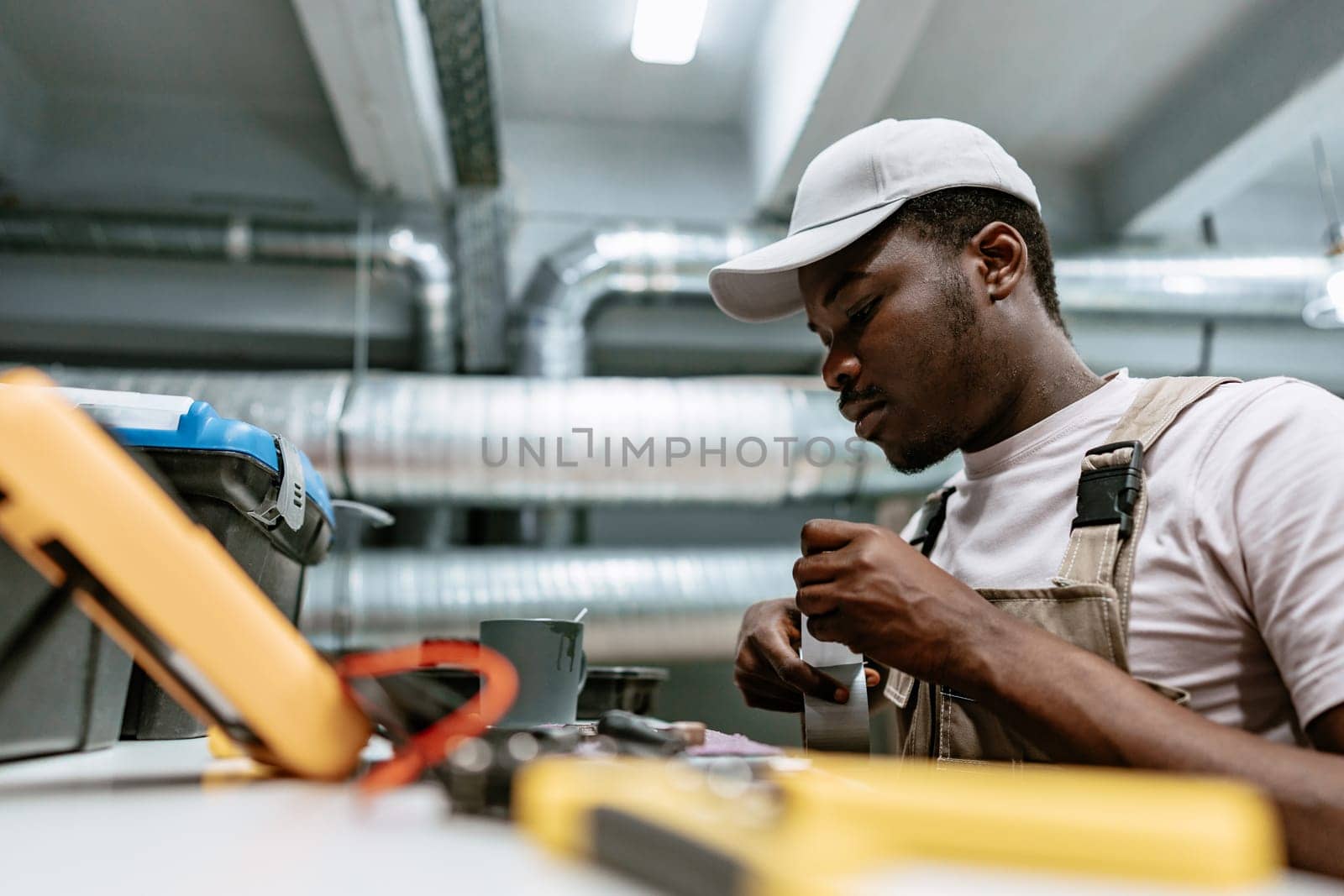 A technician focuses intently while working on electrical components in a well-equipped industrial workshop. Tools and equipment are organized on the table, indicating a detailed task at hand.