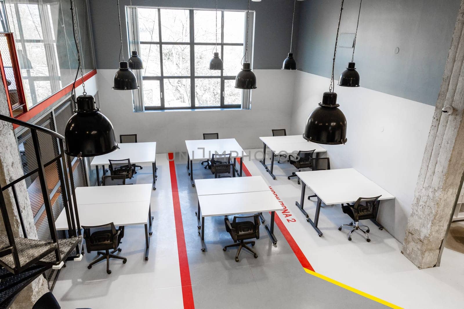 Bright, spacious workspace features several desks arranged for team collaboration. Large windows allow natural light to fill the area, enhancing productivity and creativity.
