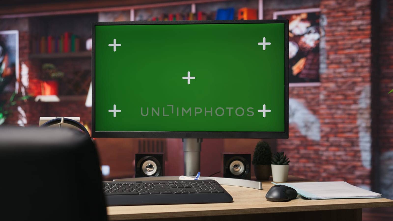 Isolated screen mockup PC on home office desk with stationary items and headphones on, surrounded by plants. Chroma key computer display in loft with shelves filled with books in background