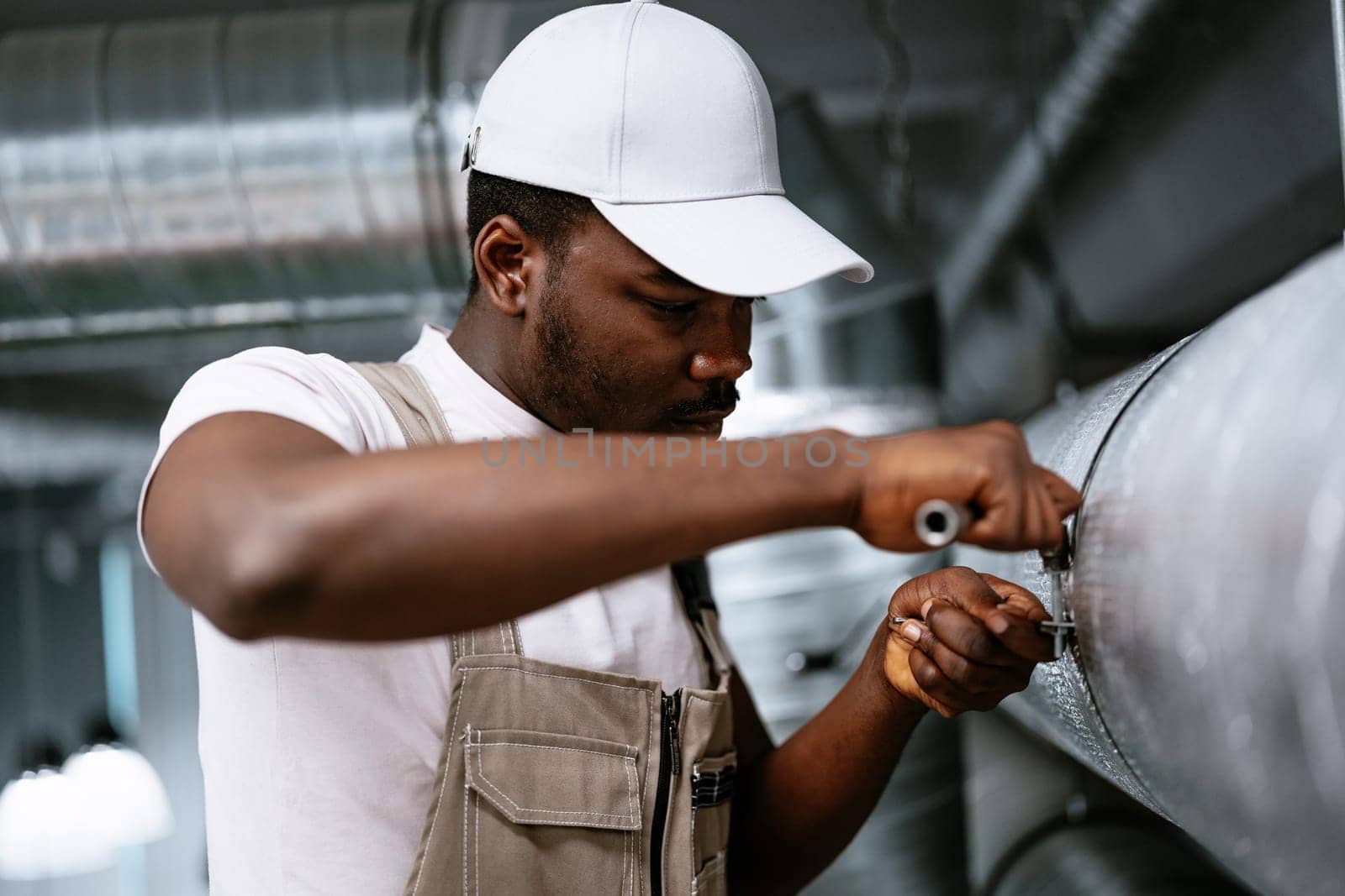 A man dressed in work attire is carefully repairing an industrial pipe.