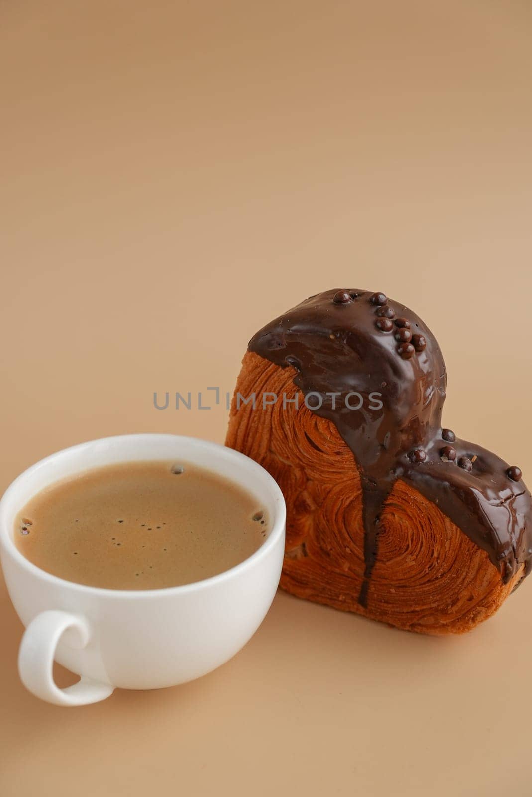Coffee latte cappuccino drink beverage morning breakfast Heart shaped dark chocolate croissant on beige background with copy space. Puff pastry new trendy sweet dessert bakery. Creamy dough experiment
