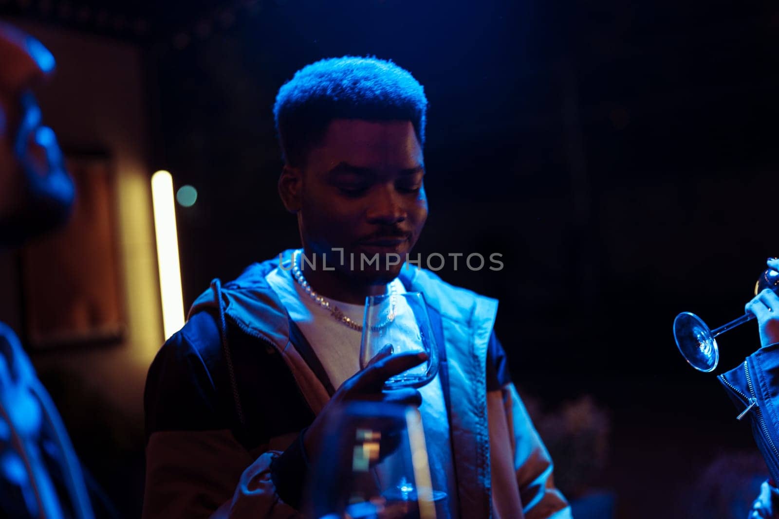 Friends socialize at a lively gathering, sipping drinks and engaging in conversation under colorful lighting. The atmosphere is warm and inviting, enhancing their connection.