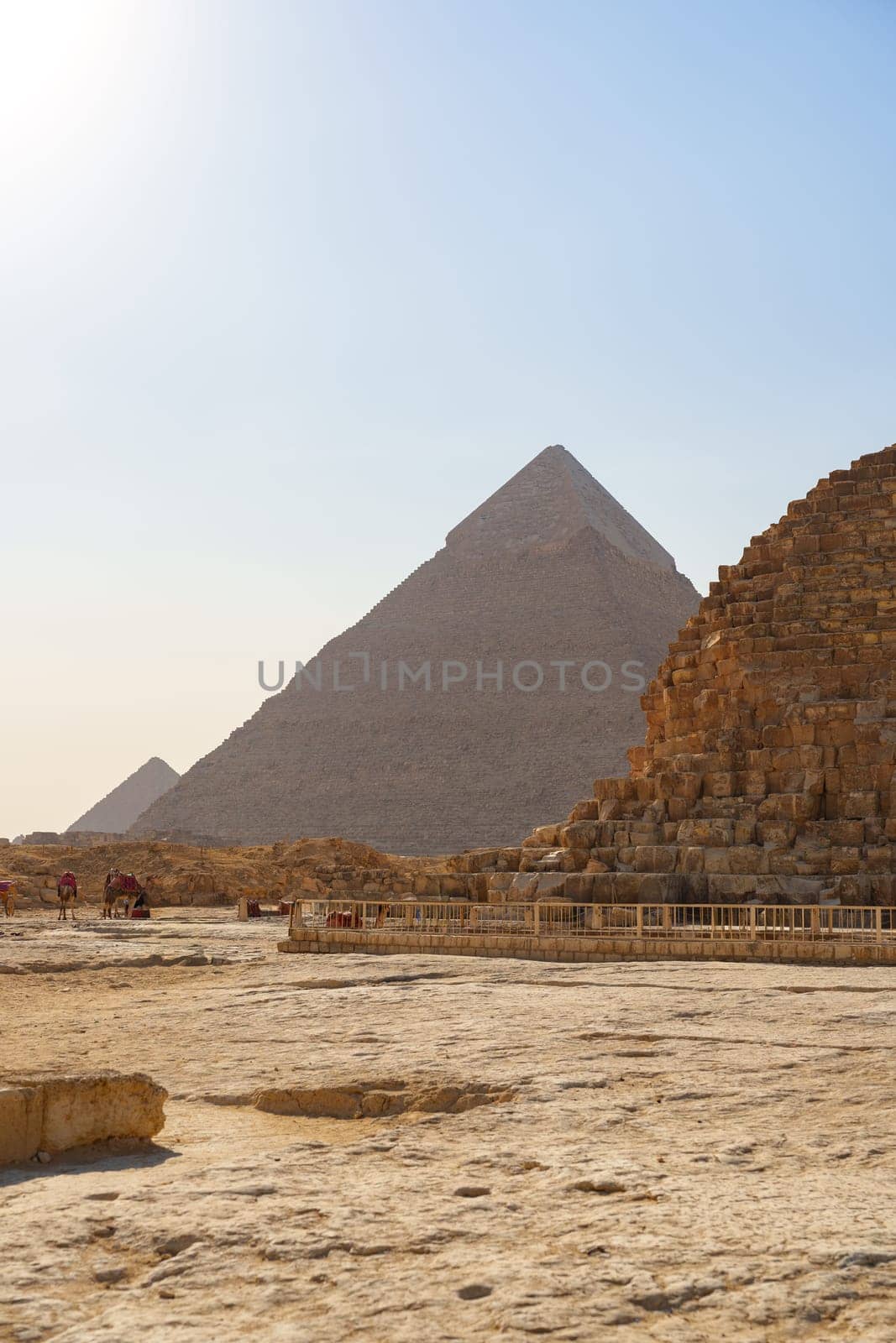 Tourists explore the historic Giza pyramids, surrounded by sandy terrain and ancient stone structures, during a sunny day in Egypt. The iconic pyramids stand proudly against the horizon.