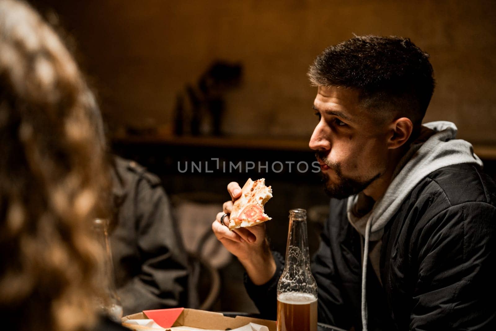 Two friends share a lighthearted moment in a warm restaurant while savoring pizza and drinks. The atmosphere is relaxed as they enjoy their meal and conversation.