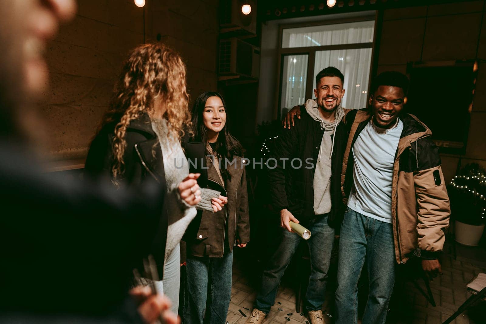 A lively group of friends shares laughter and smiles during an evening gathering in a cozy indoor setting. The ambiance is warm and inviting, filled with joy and camaraderie.