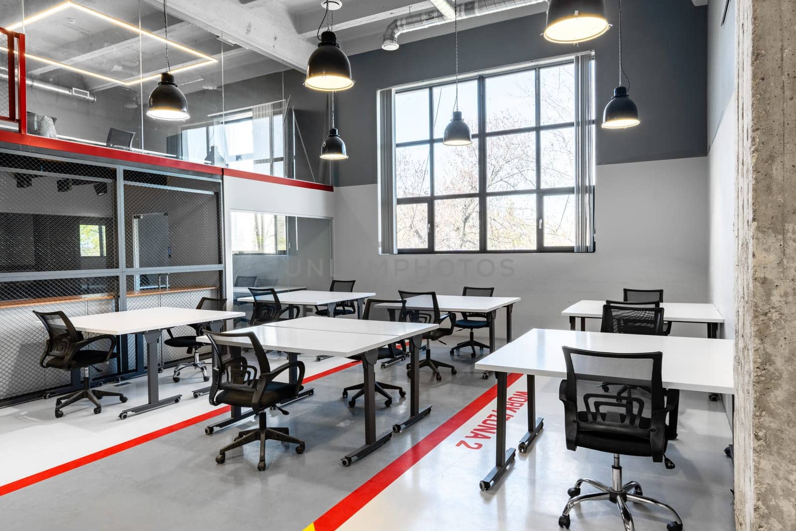 Bright and spacious coworking area showcases multiple white desks and ergonomic chairs arranged for productivity. Large windows bring in natural light, enhancing the work environment.